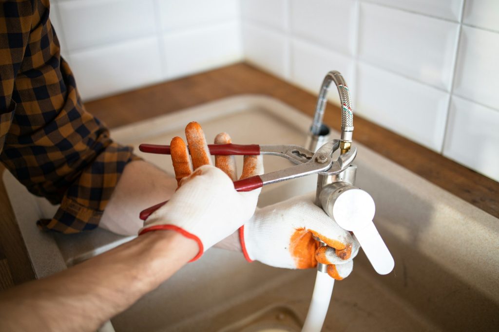 Uniformed plumber is using a wrench to repair a water pipe under the sink. Maintenance concept: elim